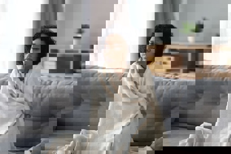 A woman is wrapped in a blanket, looking cold