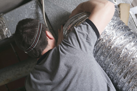 A person in a gray shirt working on ductwork