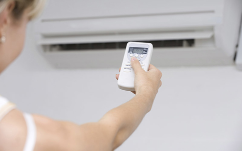 A woman pointing a remote control at air conditioner