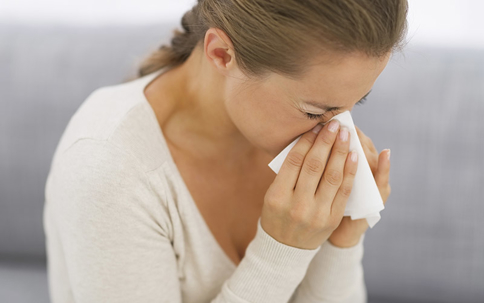 A woman holds a tissue to her nose