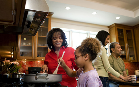 A family prepares a meal together in a warm, well-lit kitchen