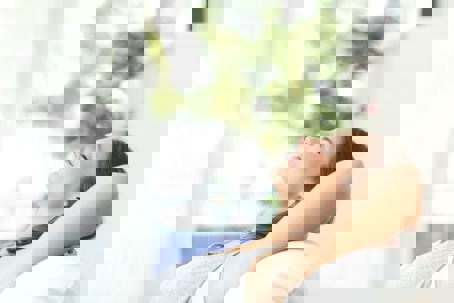 A woman sits relaxed with her head back and hands behind her neck