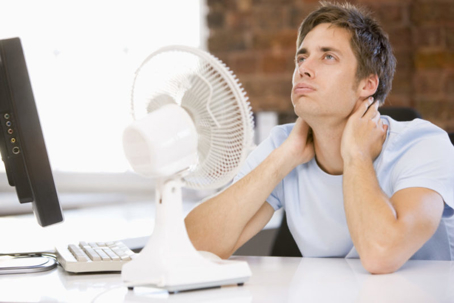 A man is trying to cool down with a desk fan