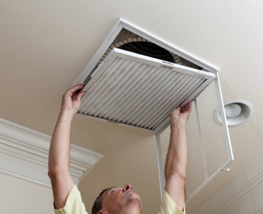 A man is changing an air filter in a ceiling vent