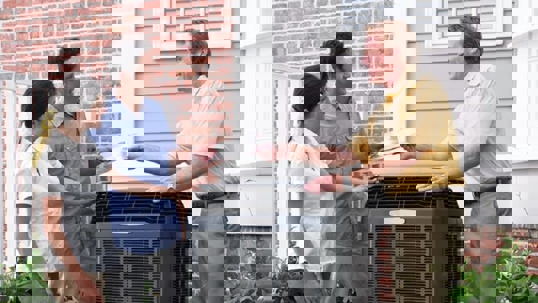 A technician explains to a couple the workings of their HVAC unit