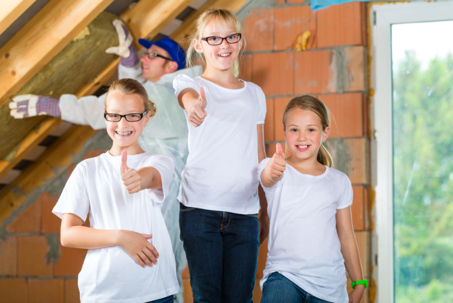 Two girls give a thumbs-up, while a construction worker installs insulation