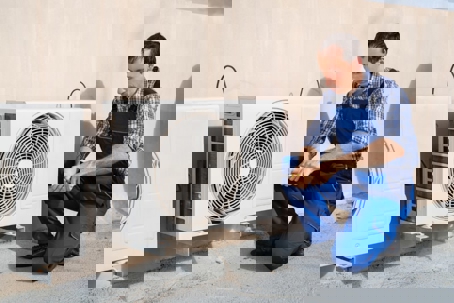 A man kneeling next to an outdoor air conditioning unit