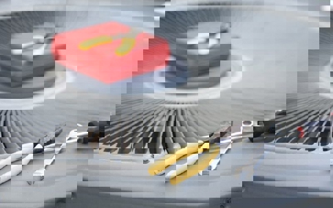 A toolbox, wrench, screwdriver, and pliers lie on a grey air conditioner unit