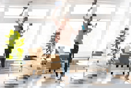 A woman cheerfully cleans a bright, modern living room