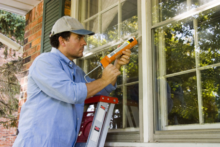 A man applies caulk around a window frame