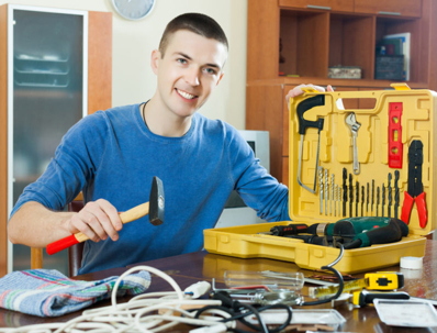 A man with a hammer poses next to a yellow toolbox
