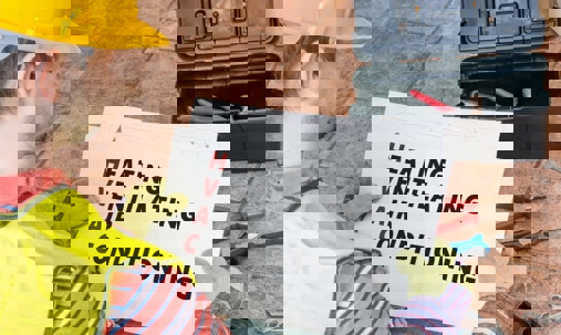 A worker kneeling next to a toolbox holds up a sign