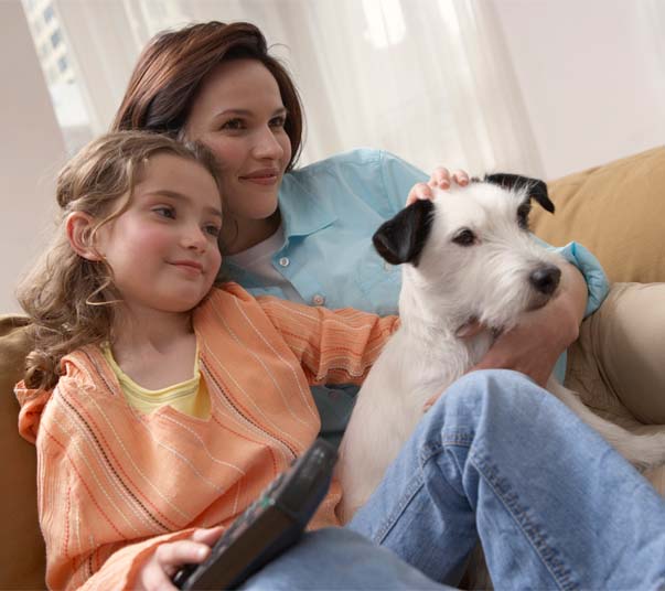 Mother, Daughter And Dog Sitting On Sofa